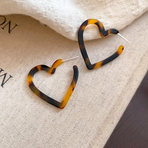 Close-up of tortoise shell resin heart-shaped earrings on a soft fabric background