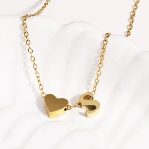 Close-up of 18k gold plated heart and letter S pendant on a white shell surface