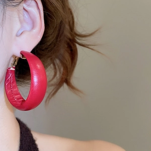 Close-up of a model wearing large red leather C-shaped hoop earrings with gold metal accents