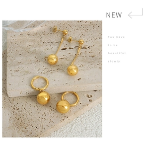 Close-up of gold plated steel ball drop earrings and tassel studs on stone pedestal