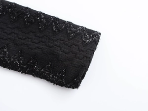 Detailed macro view of black tweed fabric texture and shiny wave embroidery on the dress sleeve