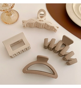 Detail view of four large milk tea colored matte hair claws in various elegant shapes