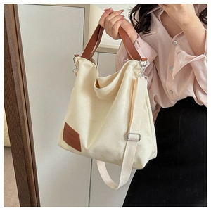 Detail of cream canvas tote bag with brown leather handles and adjustable shoulder strap