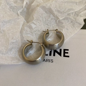 Detail view of thick silver metallic hoop earring with engraved logo on textured paper