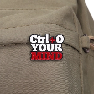 Macro shot of Ctrl + O YOUR MIND enamel pin on canvas fabric showing creative metal detail