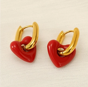 Close-up of golden huggie earrings featuring glossy red enamel heart-shaped charms