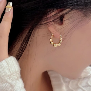 Gros plan de boucles d'oreilles créoles perlées dorées en forme de C portées par un modèle