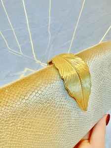 Detail of elegant gold feather clasp and textured surface on evening clutch bag