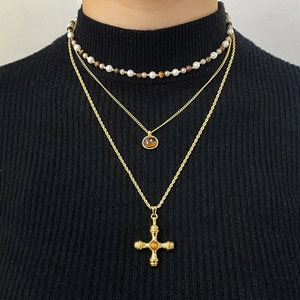 Three-layer gold necklace set with tiger eye stones and cross pendant on a black sweater