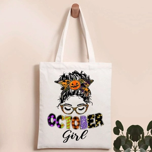 Close-up of white canvas tote bag featuring Halloween October Girl pumpkin print on a hook