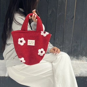 Detail of red felt tote bag with 3D plush flower applique and brand label on front