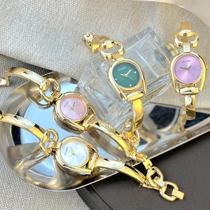 Detail of four golden bangle watches with green purple pink and white dials on gold tray