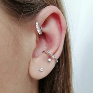 Detail of silver S925 earrings set with zirconia and twist texture on human ear