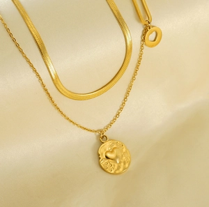 Macro shot of double-layer gold necklace with flat snake chain and heart pendant on satin
