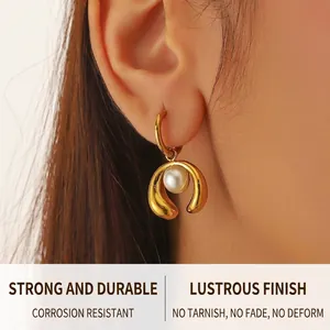 Detail view of a gold horseshoe earring with a white pearl on a model's ear lobe