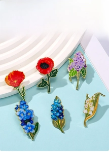 Flat lay of five floral enamel pins including lily of the valley and poppy on blue base