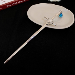 Close-up of silver sword hair pin with blue teardrop gem on a white ceramic tray