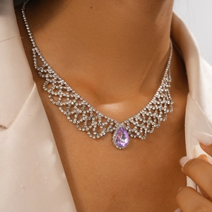 Close-up of a silver mesh necklace with a purple teardrop pendant and crystal inlay