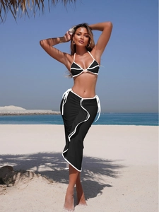 Three-piece black bikini set with white wave trim and a side-tie beach skirt on a sunny beach