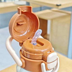 Detail of coffee-colored pop-up lid with silicone straw and cream-white handle