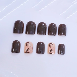 Short square press-on nails in chocolate brown with leaf patterns and gold glitter detail