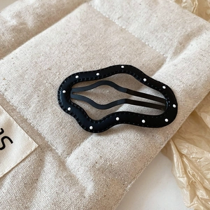 Close-up of black wave-edged hair clip with white polka dots on a textured fabric