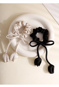 Detail of tulip tassel silk scrunchies in black and beige on a ceramic plate
