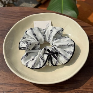 Detail of satin scrunchie with musical notes pattern and a small black ribbon bow