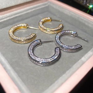 Detailed view of C-shaped zircon earrings in gold and silver finish on velvet