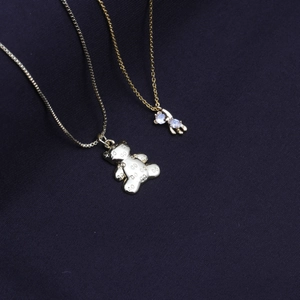 Golden teddy bear pendant necklace with GO pattern and gemstone charm on blue background