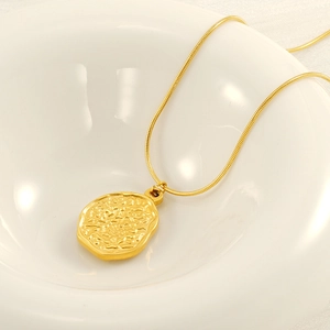 Collier chaîne serpent dorée chic avec un pendentif ovale martelé irrégulier dans un bol blanc