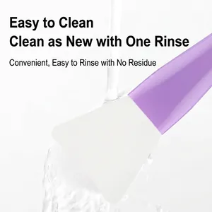 Silicone face mask applicator brush with white fan head being rinsed under water stream