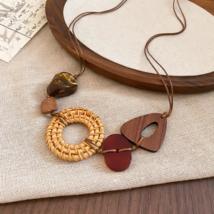 Close-up of bohemian woven rattan and resin triangle pendant necklace on a wooden tray