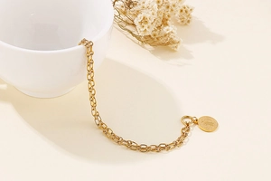 Close-up of a double-layer gold coin bracelet draped over a white ceramic cup