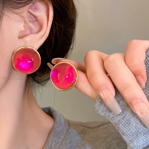 Detail of round magenta earrings with gold frame on model, showing texture and size