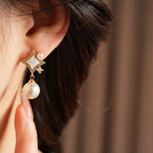 Vue détaillée des boucles d'oreilles perles avec cadres en or étoilés et zircons