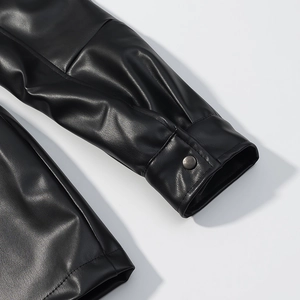 Détail de la manche en cuir noir brillant avec bouton-pression métallique et texture fine