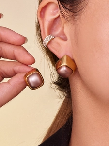 Close-up of geometric gold-matte pearl earrings and a crystal ear cuff on model