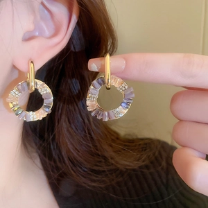 Detail showing crystal-encrusted geometric gold hoop earrings on ear with purple gems