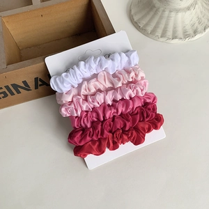 Detailed view of five gradient satin scrunchies in shades of pink on a white display card