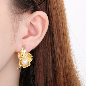 Gros plan de boucles d'oreilles fleur plissée plaqué or 18k avec perle blanche sur oreille