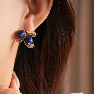 Close-up of vintage gold hollowed floral earrings with navy blue lapis lazuli stones