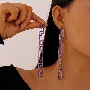 Detailed view of long geometric tassel earrings with purple crystals and Greek key pattern