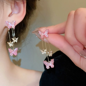 Boucles d'oreilles papillon dorées avec pompons et zircons roses sur un mannequin