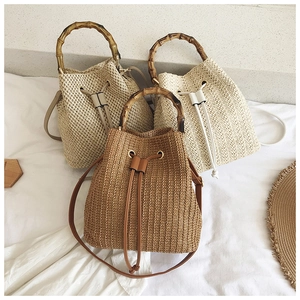 Straw bucket bags with bamboo handles in brown and cream colors on white fabric
