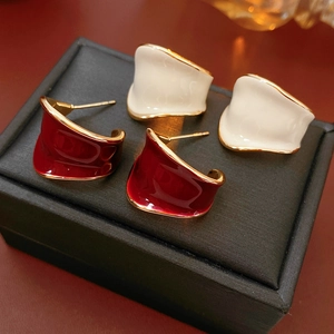 Dettaglio di orecchini a smalto rosso e bianco a forma di C con bordo dorato su box