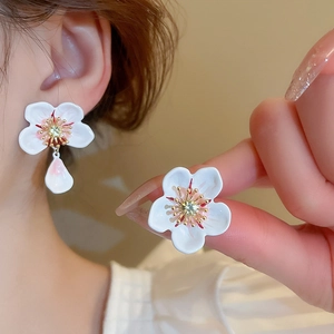Detail of asymmetrical floral earrings with inlaid yellow gemstone and pearl-like finish
