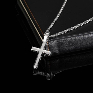 Iced out silver cross pendant necklace with rope chain on black reflective surface
