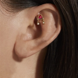Detail of a gold triangle cartilage stud with a red gemstone and two diamond charms