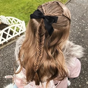 Detail of a black satin double bow hair clip styled on an intricate braided hairstyle